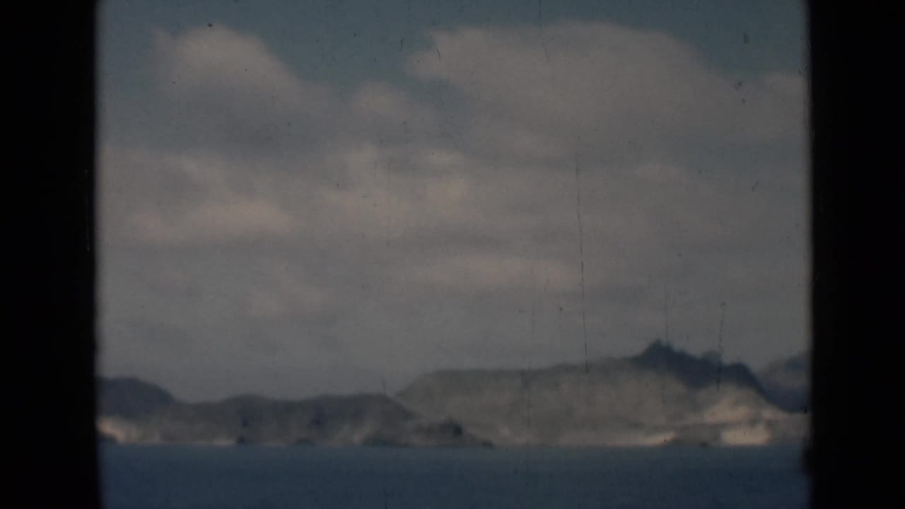 Distant cliffs and shoreline beyond calm ocean, with dark vertical borders in the frame.