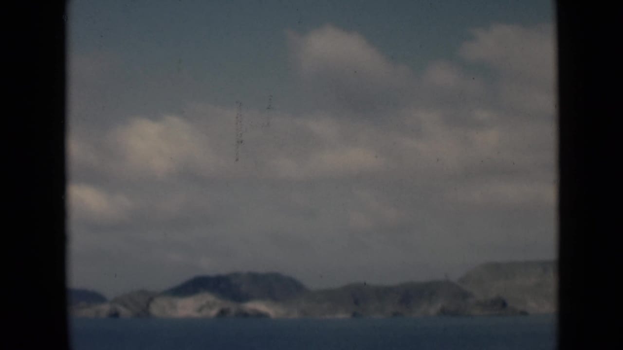 Low mountain ridges across calm blue water with clouds overhead and a dark central divider.