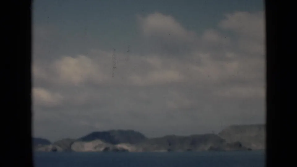 Archival 8mm frame showing distant coastal ridges, calm sea, and cloud cover, with Aden, Yemen indicated by clip metadata.