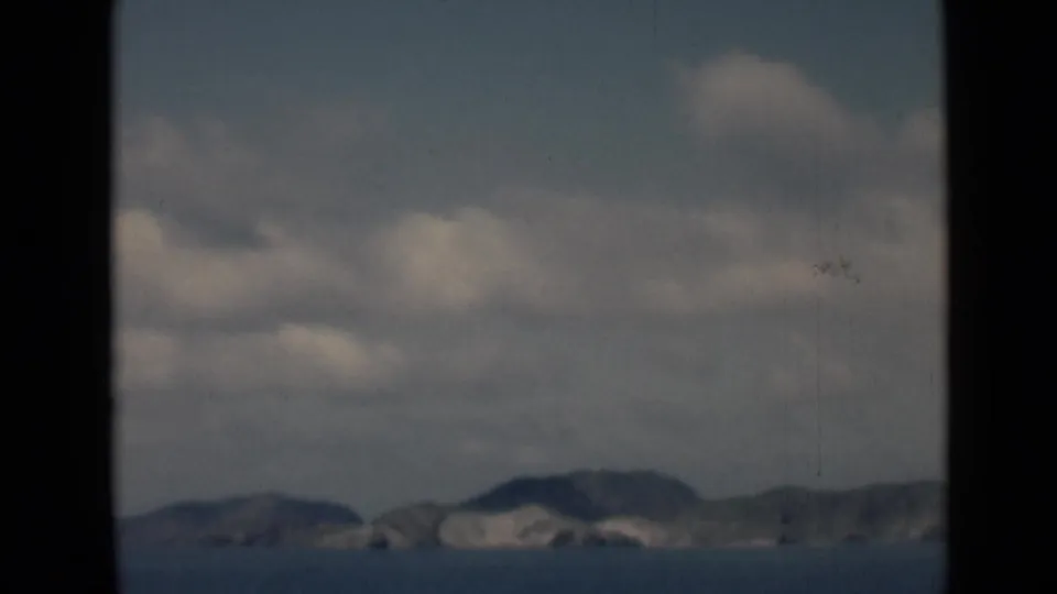 End frame of the 8mm clip with distant coastal hills, blue sea, soft clouds, and visible film wear.