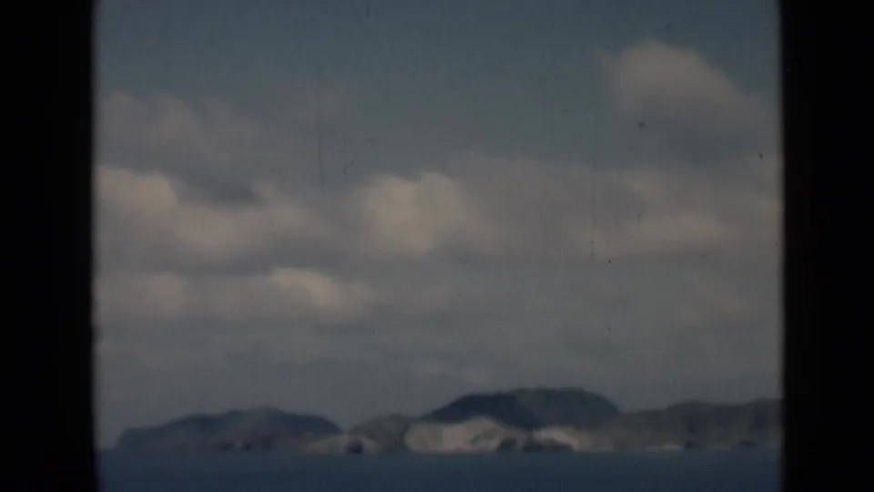 1946 8mm home-movie frame associated with Aden, Yemen, showing distant mountains across calm water beneath soft clouds.
