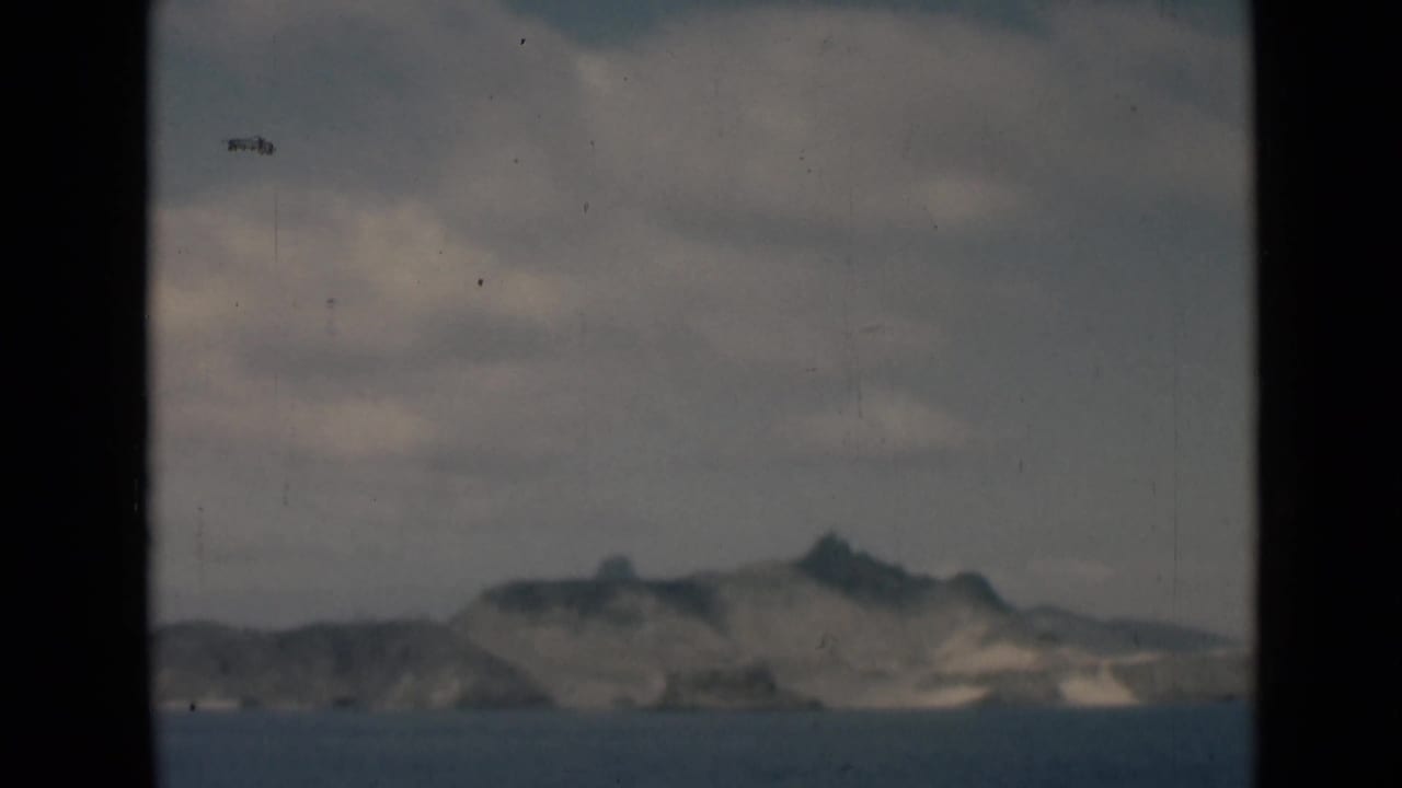 Mountainous coastline across calm water, divided by dark vertical window bars.