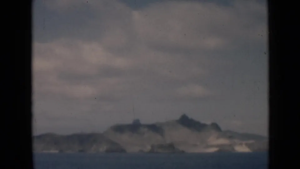 Aden-associated 1946 home-movie frame with distant rugged hills across water, softened by grain and slight blur.