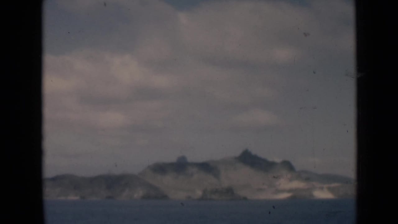 Distant rocky island across calm water beneath layered clouds.