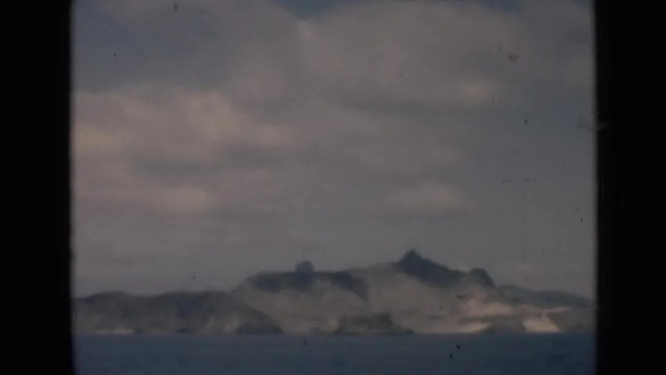 1946 8mm view of a distant barren island or coastal ridge across calm sea under muted cloud cover.