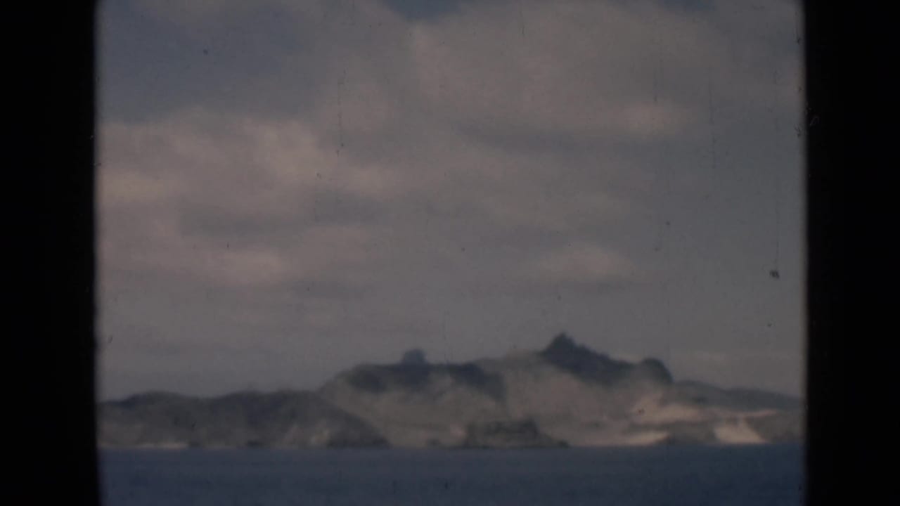 Rocky island profile across blue water with cloudy sky above.