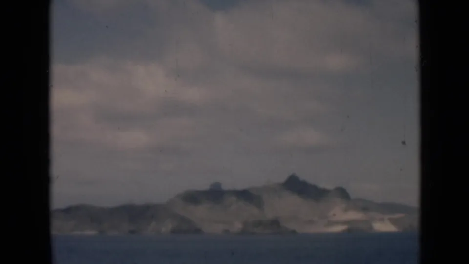Distant island profile in a 1946 8mm maritime view, with muted blue water and broad gray clouds.