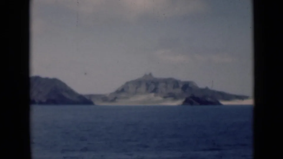 A larger rocky island fills more of the frame, with calm water in the foreground and the smaller landform partly cropped at left.