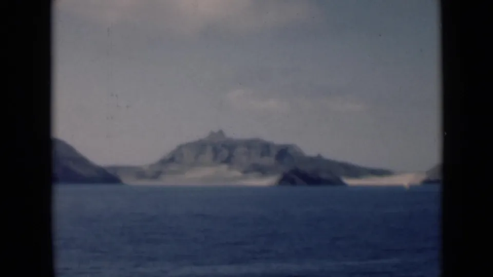 The final frame shows the rocky ridge, a small dark outcrop near shore, blue water, and soft faded 8mm texture.