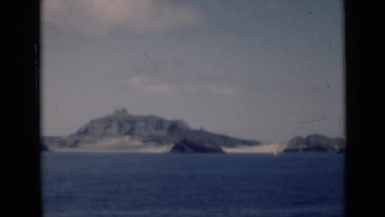 Rugged island shoreline seen across open water with dark film borders.