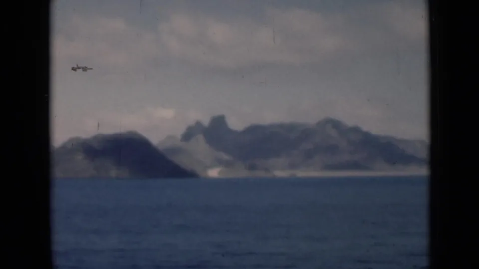 1946 home-movie frame showing a mountainous coastal landmass beyond calm blue water, with soft focus and visible film wear.