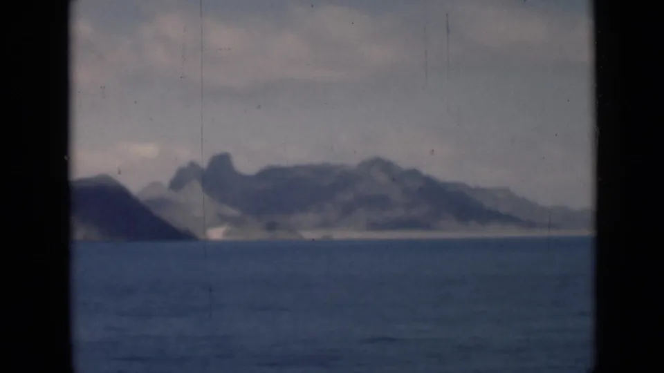 A later 8mm frame shows hazy coastal mountains, blue sea, and pale shoreline, consistent with a passing shipboard view.