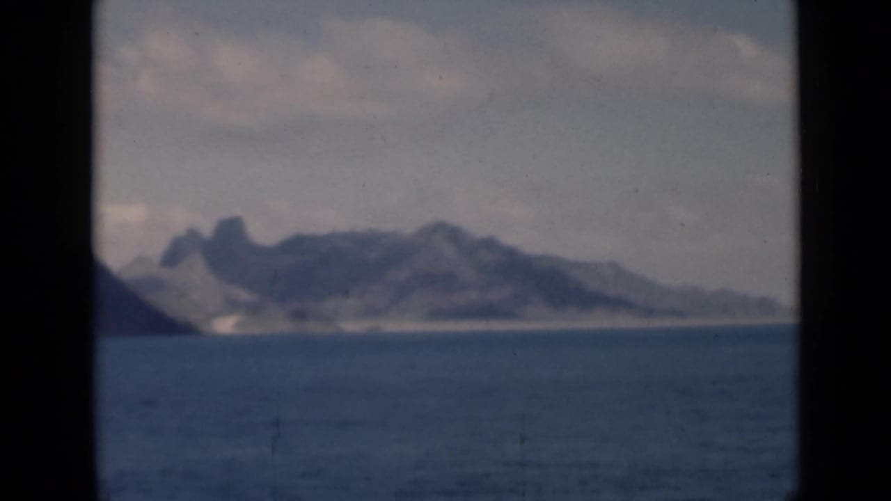 Distant mountain coastline across calm blue water under a cloudy sky.