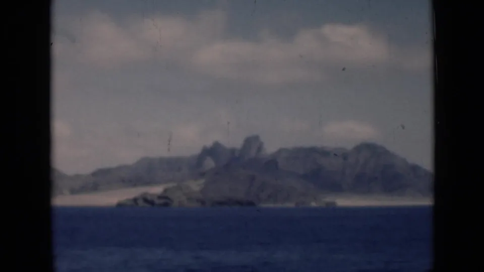 Coastal headland and jagged mountain peaks viewed across dark blue water in archival 1946 8mm travel footage.