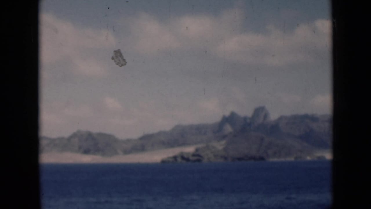 Hazy coastal mountains and dunes beyond open sea with dark vertical film borders.