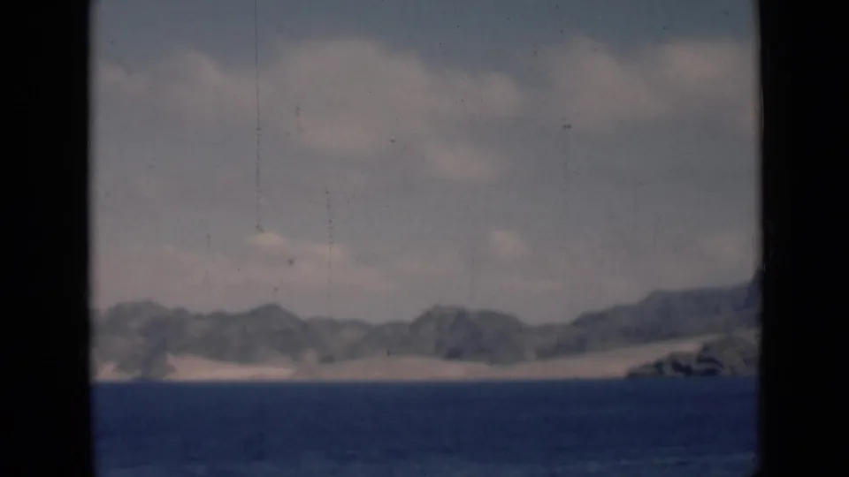 A wide 1946 8mm frame shows an Aden/Yemen-associated coastal horizon with blue sea, pale dunes, low rugged mountains, and scan scratches.