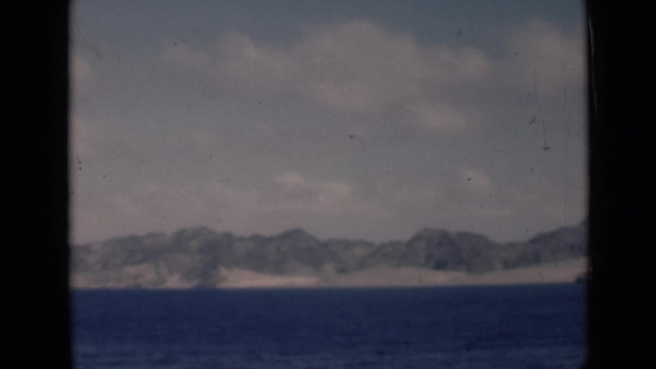 Low mountain range beyond a sandy coast, seen across dark blue water.