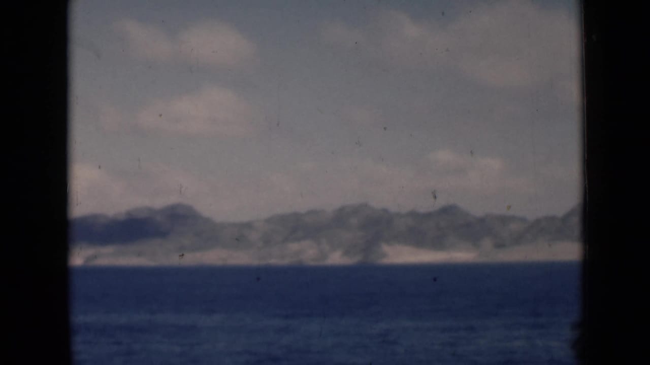 Blue sea with a distant mountainous coastline under a cloudy sky.