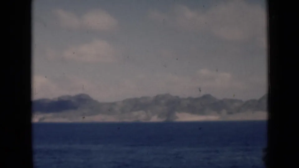 Passenger-view 8mm frame of open water and a hazy mountain coastline, consistent with the clip's 1940s travel-reel metadata.