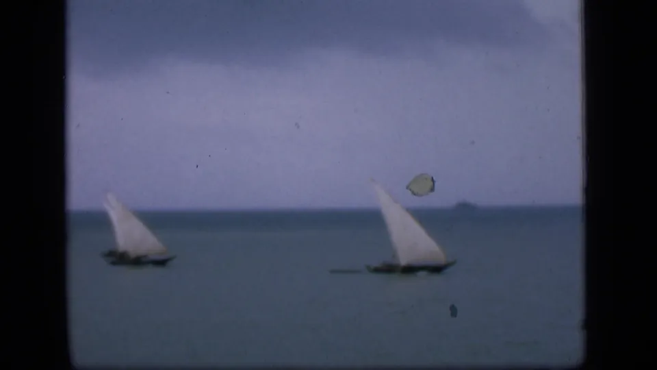 Bombay coastal water scene with two traditional sailboats moving across a calm sea under a hazy sky.