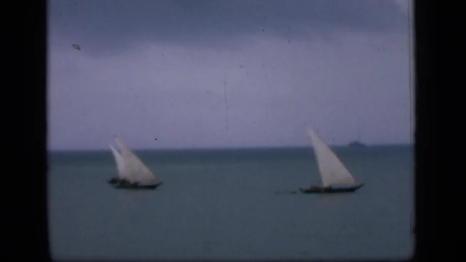 Wide 8mm view of two sailboats on Bombay coastal waters, framed by faded color and visible film borders.