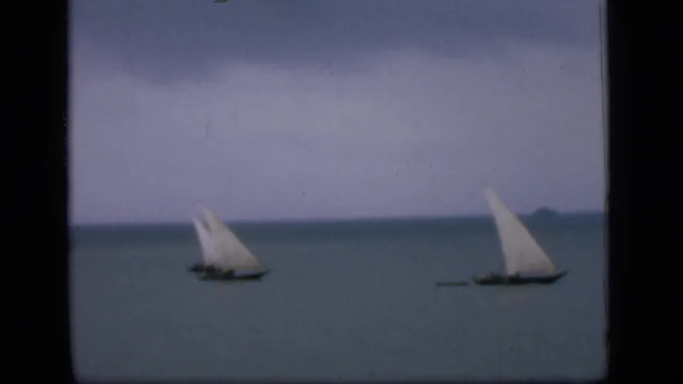 1946 Bombay home-movie frame showing distant small sailboats on calm ocean water beneath a muted horizon.
