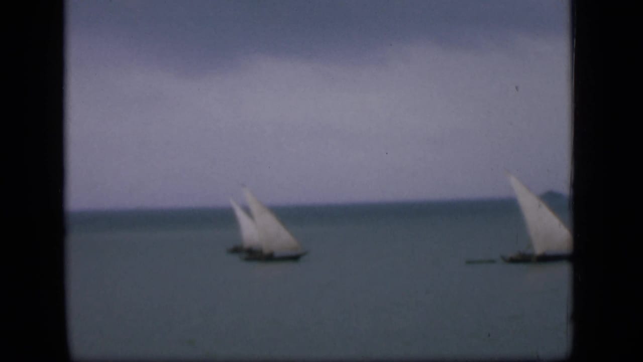 Distant sailboats crossing calm water, partly framed by dark vertical film borders.