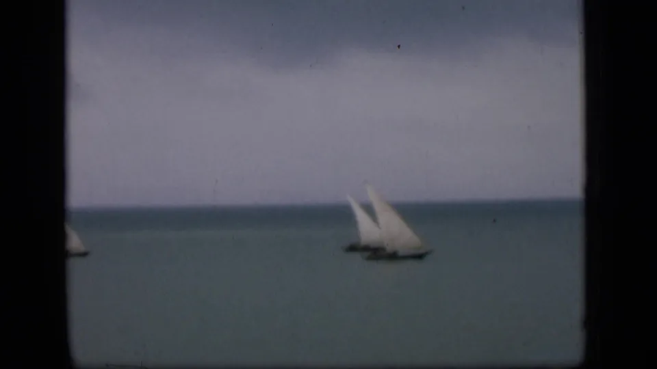 Soft 8mm view of a distant sailboat on calm water near Bombay, with dark film borders visible.