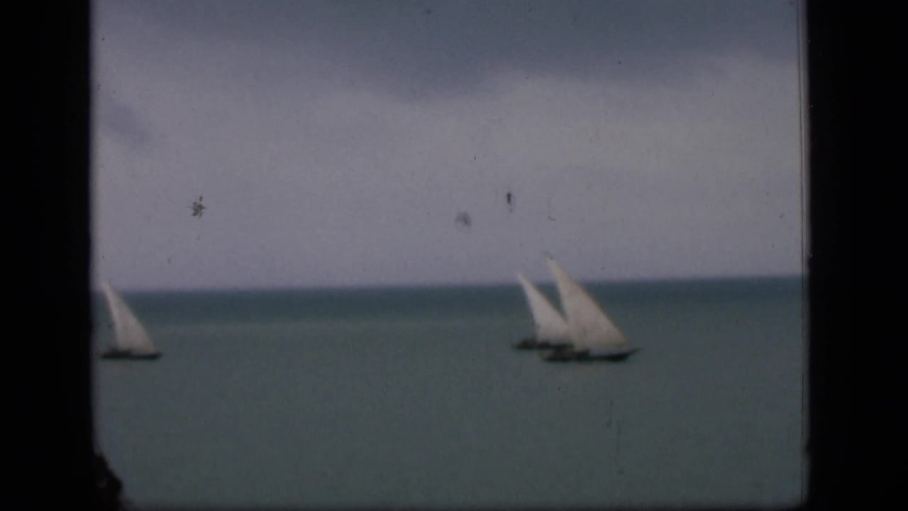 1946 Bombay home-movie frame showing distant white-sailed boats on calm water with visible 8mm gate edges and film wear.