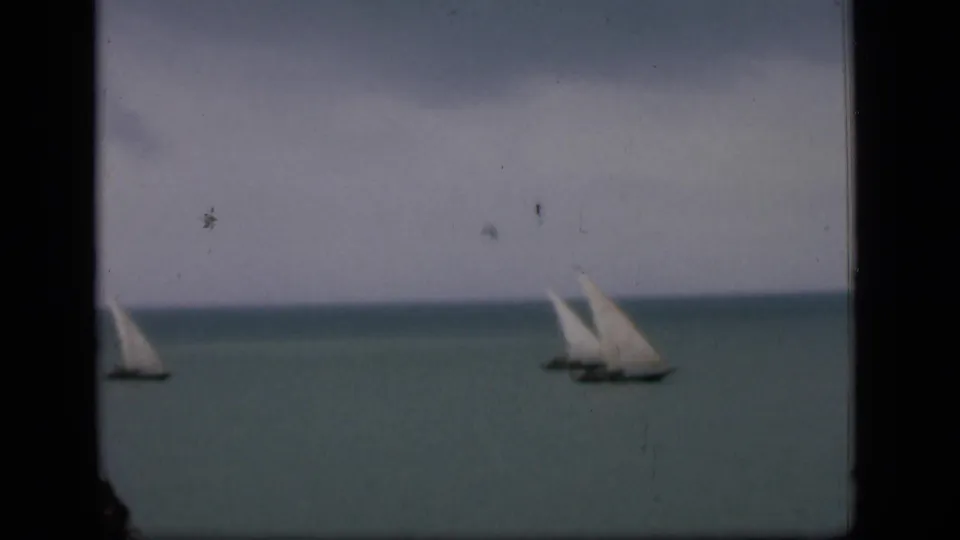 1946 Bombay home-movie frame showing distant white-sailed boats on calm water with visible 8mm gate edges and film wear.