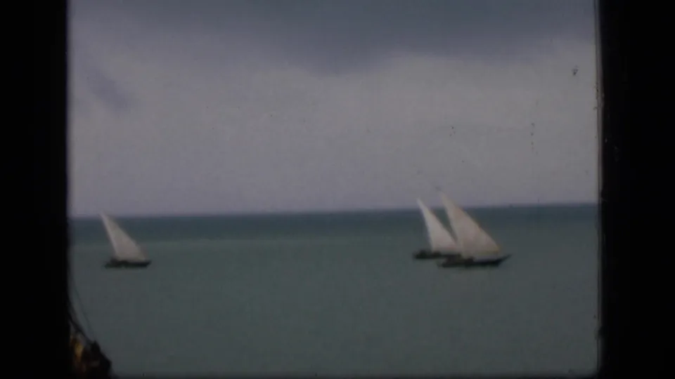 A 1946 Bombay coastal frame with two distant sailboats, soft color, low horizon, and dark 8mm frame edges.