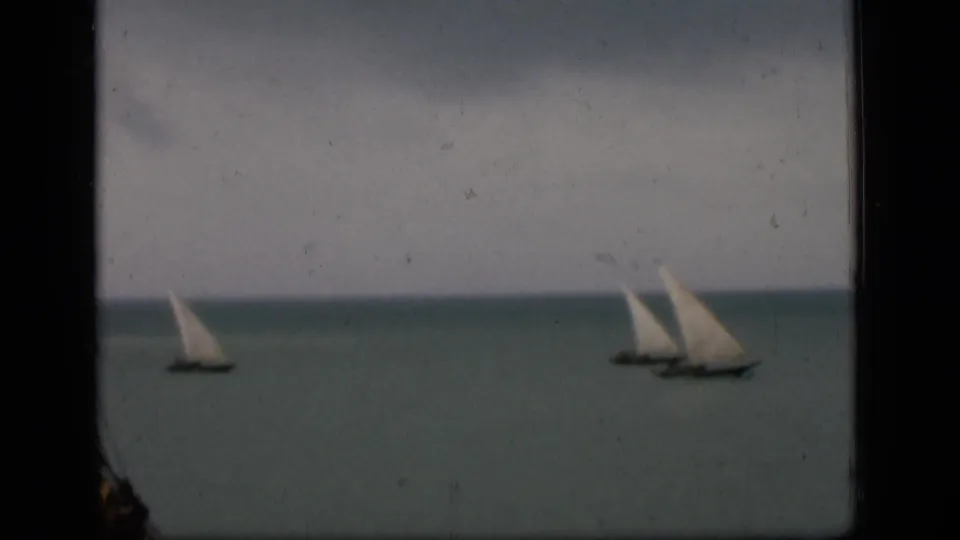 Final 1946 Bombay frame showing white-sailed boats on muted water, with scratches, dust marks, and dark gate edges.