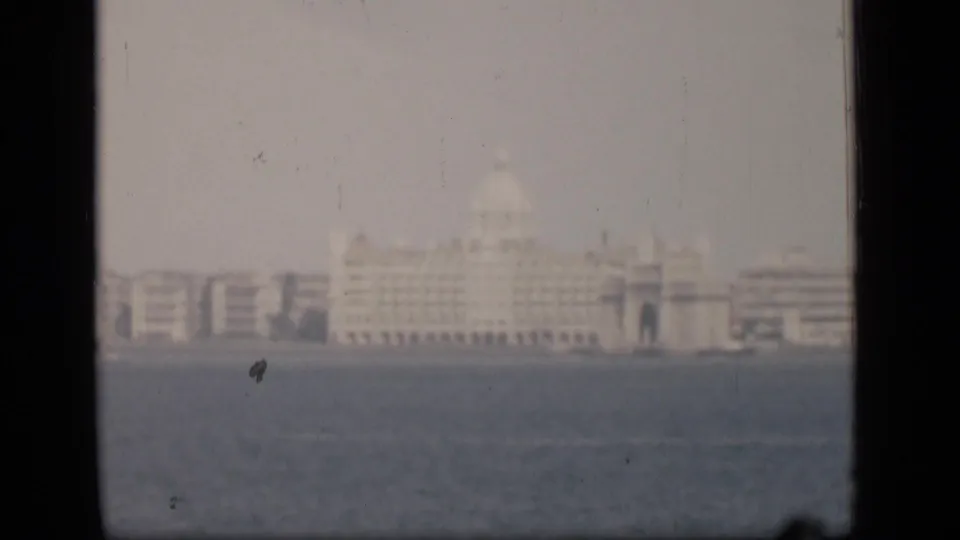Misty 1946 Bombay waterfront scene with a distant hotel-like landmark and surrounding buildings across the water.