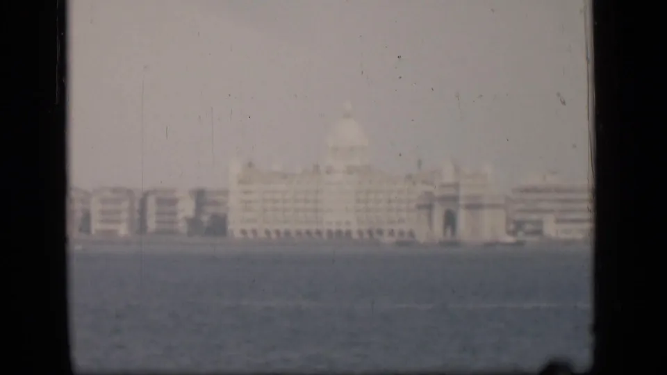Final 1946 Bombay frame showing the pale waterfront landmark and adjacent buildings through haze and film wear.