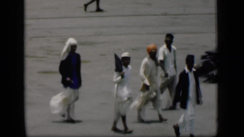 1946 Bombay 8mm frame showing several people in traditional attire walking across open pavement.
