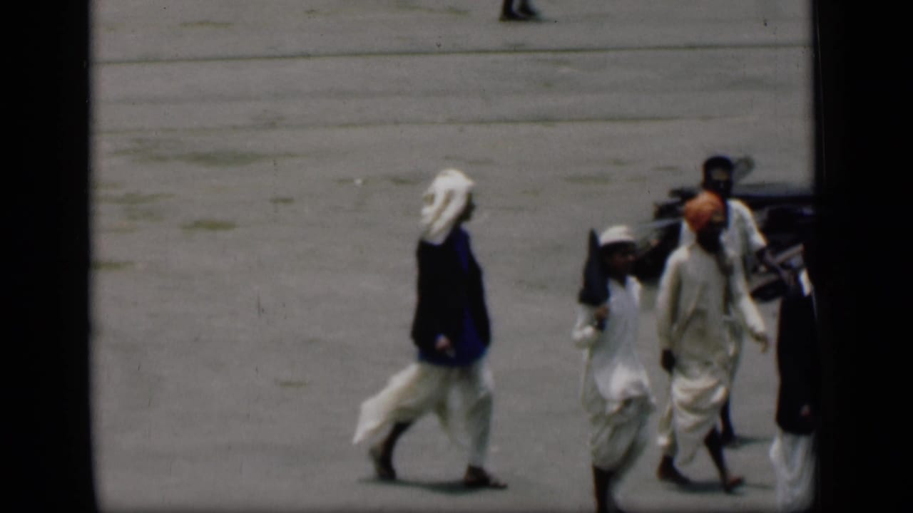 Men in white garments and turbans walk across pavement near a dark vertical edge.