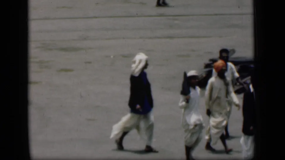 1946 Bombay home-movie frame with men in white clothing and turbans moving through a paved public area.