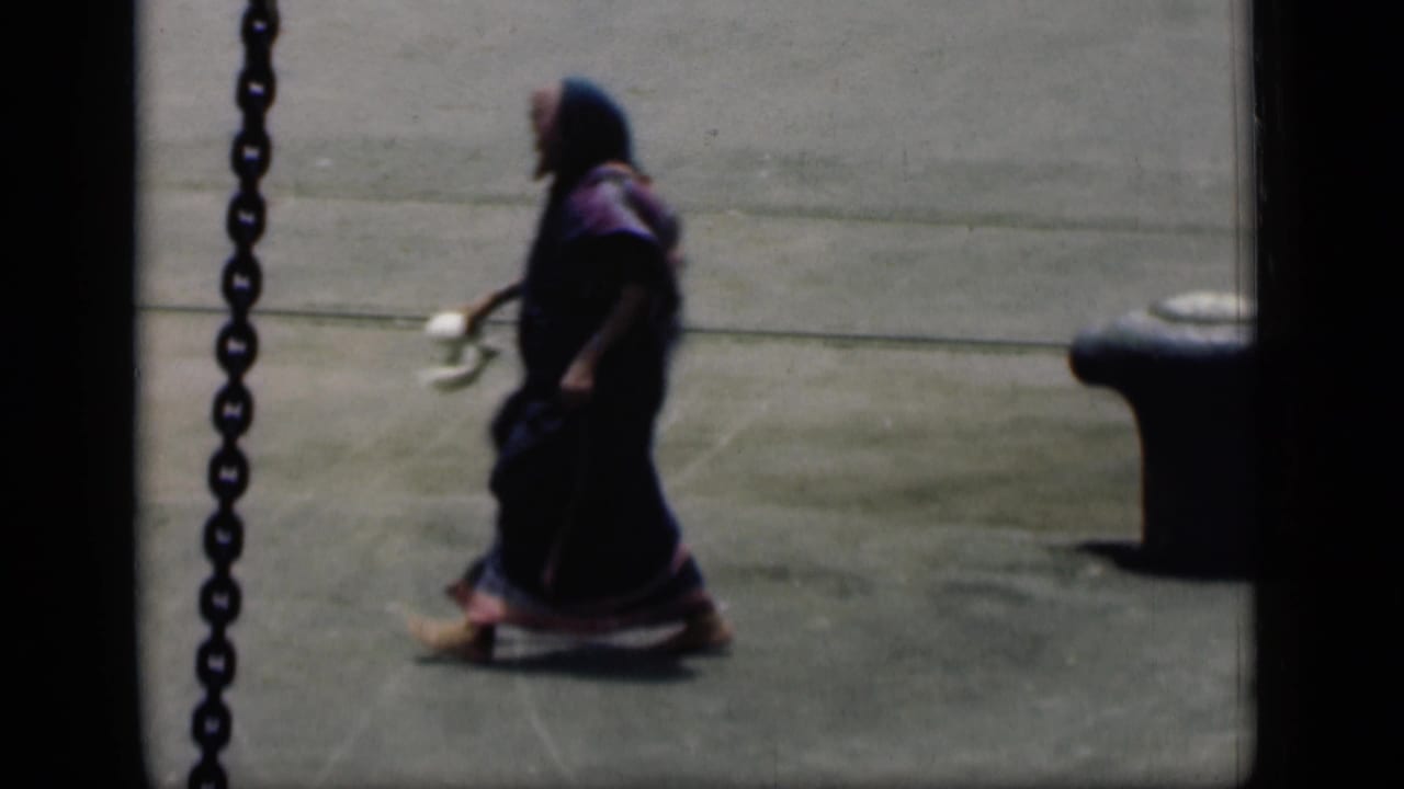 Woman in a dark sari walks across a paved street surface near a chain and curb.