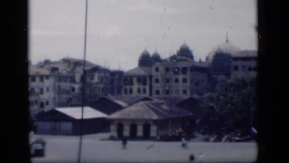 1946 Bombay view across an open plaza toward domed colonial-era buildings, with trees and distant pedestrians.