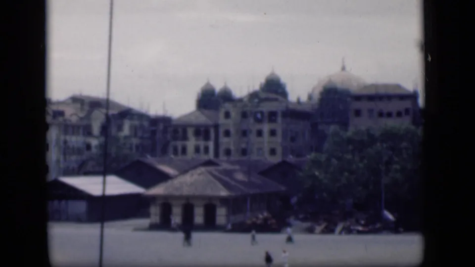 Wide 1946 Bombay plaza scene with domed architecture, foreground roofs, trees, and small walking figures.