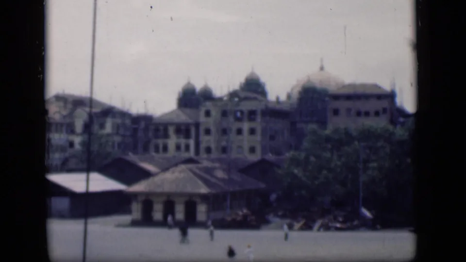 1946 Bombay plaza view with a small roofed structure in front of domed buildings and pedestrians crossing the open ground.