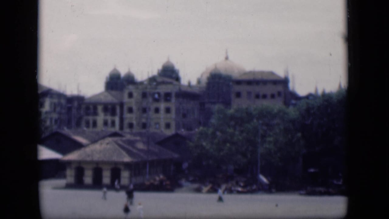 Distant domed building behind trees with pedestrians crossing an open paved area.