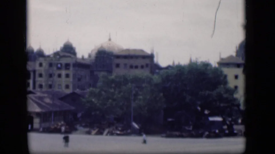 1946 Bombay cityscape on 8mm, showing domed buildings behind trees and a wide open area with tiny indistinct figures.