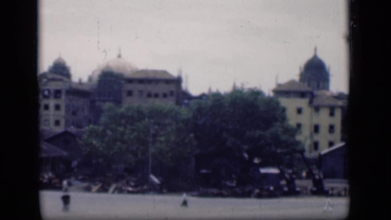 Soft city skyline with domes, trees, open ground, and small distant figures.