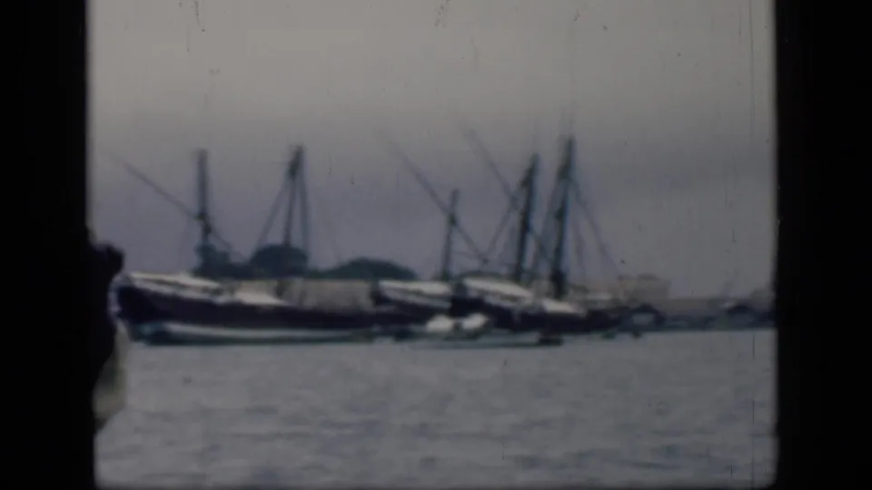 Hazy 1946 Bombay harbor view with moored boats, tall masts, and water filling the foreground.