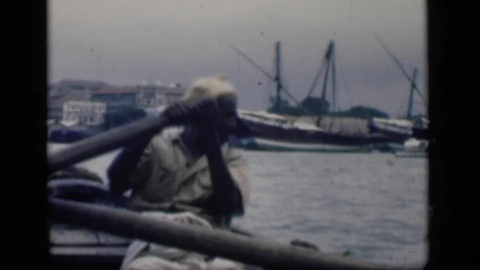 The 1946 Bombay harbor view shows the rower leaning beside an oar or rail, with calm water and moored masted boats beyond.