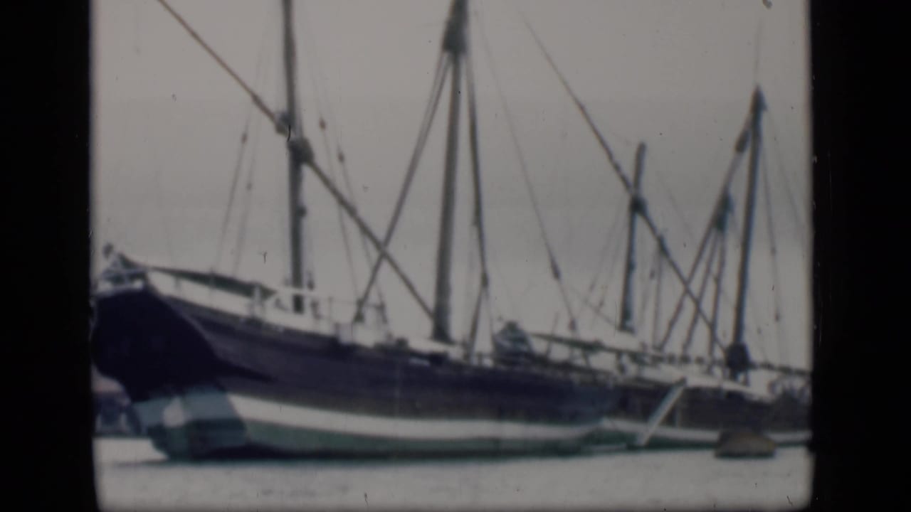 1946 Bombay home-movie frame showing a large blue and white sailing ship with tall masts and rigging at the waterfront.