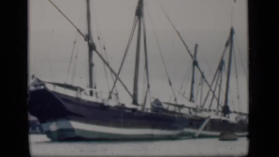 1946 Bombay home-movie frame showing a large blue and white sailing ship with tall masts and rigging at the waterfront.