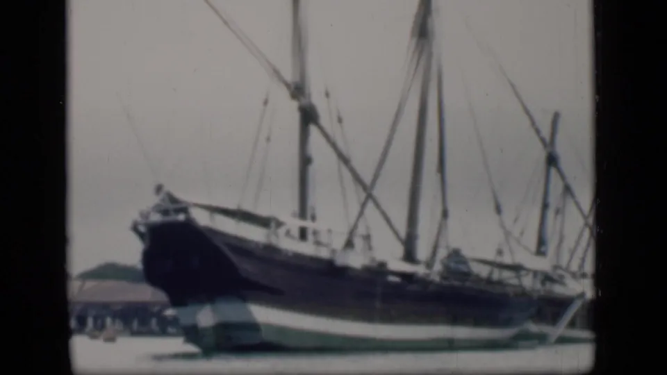1946 Bombay home-movie view of the sailing ship from the side, showing the long hull, mast lines, and dockside water.