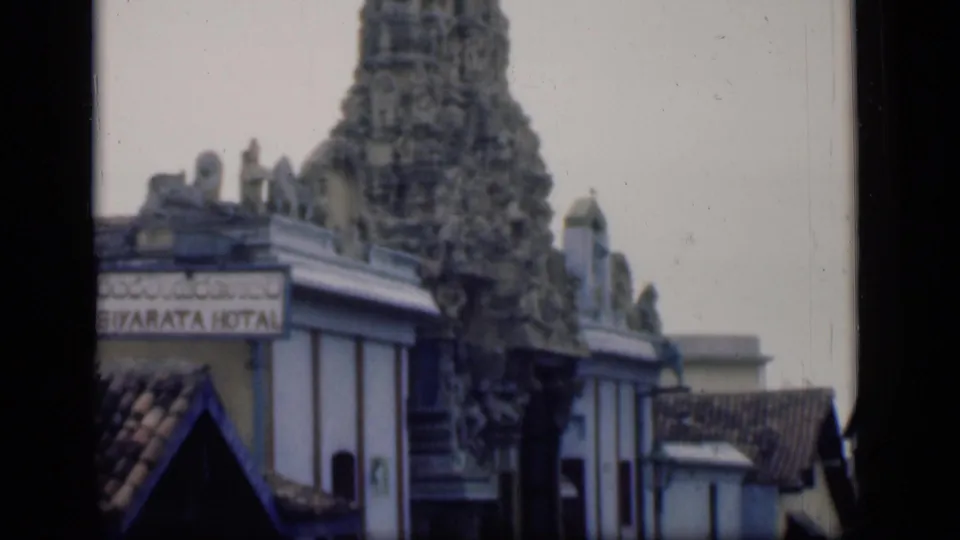 1946 Bombay view of a carved temple tower beside low urban buildings and a partially readable hotel sign.